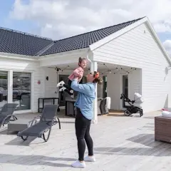 En kvinna lyfter sitt barn på en altan vid ett modernt hus, en idyllisk semesterbild från ett resort i Sverige.