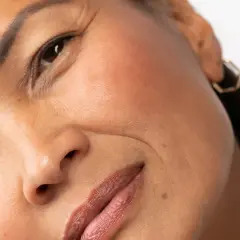 Primer plano de un rostro femenino, mostrando los signos de envejecimiento de la piel, como arrugas finas alrededor de los ojos y la boca.