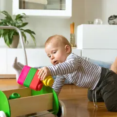 Radosne zabawy z 8 miesięcznym dzieckiem i jego nowym wózkiem-chodzikiem. Maluch z fascynacją wkłada kolorowe klocki do drewnianej skrzyni.