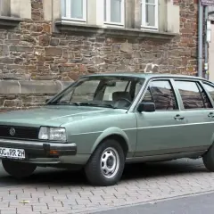 Zielonawy Volkswagen Passat, klasyk z lat 80., parkuje przed kamiennym budynkiem.