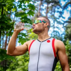 Mężczyzna w sportowym stroju pije wodę z butelki, co pić podczas treningu w plenerze.