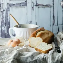 Pan brioche para torrijas, huevos y batidor sobre mesa rústica.