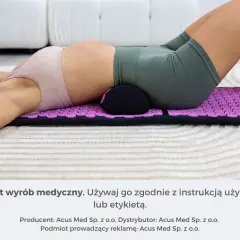 Osoba z bólem kręgosłupa lędźwiowego leży na macie akupresurowej z wałkiem pod odcinkiem lędźwiowym.