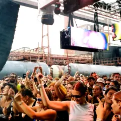 Folla in estasi sotto enormi casse, luci psichedeliche e schermi vibranti. L'energia della techno musica pervade l'aria.