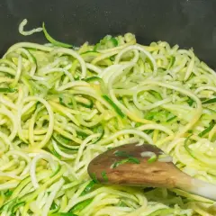 Makaron z cukinii w patelni, mieszany drewnianą łyżką. Zdrowy i lekki posiłek w przygotowaniu.