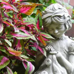 Ein Stein-Gartenzwerg, der ein kleines Bündel hält, steht zwischen bunten Blättern.