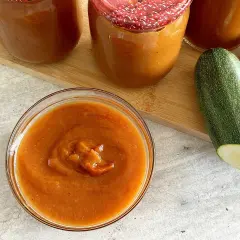 Domowy ketchup z cukinii siostry Anastazji w słoikach i miseczce, obok świeże cukinie.