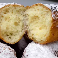 Puszyste oponki serowe, przekrojone na pół, obficie posypane cukrem pudrem. Widać ich delikatne, pęcherzykowate wnętrze.