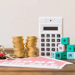 Calculadora, monedas y llaves junto a dados con números y símbolos matemáticos, sugiriendo el cálculo del valor de mercado de un inmueble.