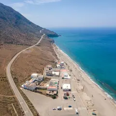 Vista aérea de la playa de la Almadraba en Almería, con el mar azul intenso, la arena dorada y un pueblo costero.