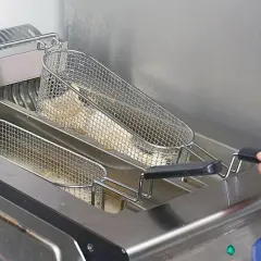 Frytki smażące się w metalowych koszach we frytkownicy.