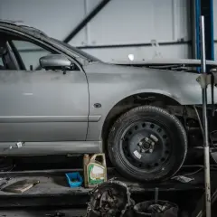 Voiture argentée en réparation dans un garage, avec des outils et une boîte d'huile. Le frein à main est prêt pour le prochain contrôle.
