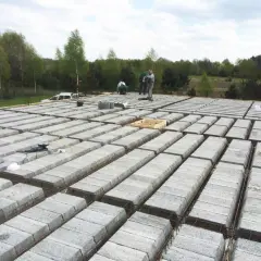 Budowa stropu teriva w toku. Betonowe pustaki ułożone w rzędach, zbrojenie gotowe do zalania. Pracownicy doglądają postępu prac.