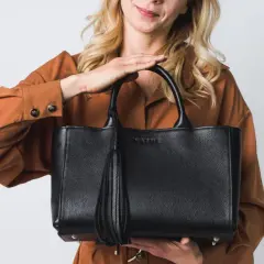 Elegancka, czarna torebka z frędzlem, idealna jako modne torebki na lato. Kobieta w rudym kombinezonie prezentuje stylowy dodatek.