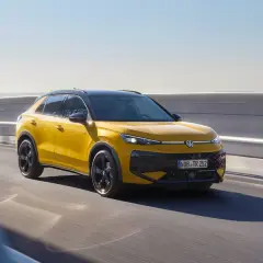 Żółty Volkswagen Cross pędzi po drodze, błyszcząc w słońcu.