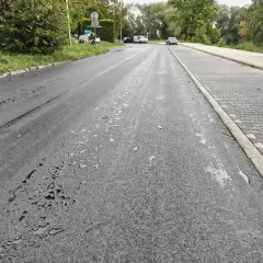 Droga w Cieszynie po deszczu, z kałużami na asfalcie i nowym chodnikiem z kostki.