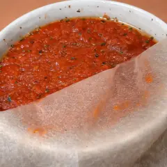 Un tazón blanco con la mejor salsa de tomate para pizza, con hierbas y un trozo de papel de arroz.