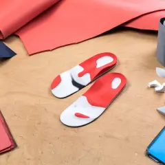 Fertigung von orthopädischen Schuheinlagen: Materialien wie roter und blauer Schaumstoff, Maßband und Werkzeuge liegen bereit.