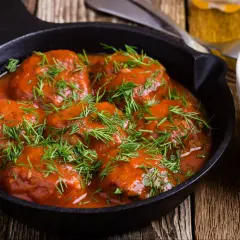 Pyszne pulpety w sosie pomidorowym, posypane świeżym koperkiem, podane w żeliwnej patelni.