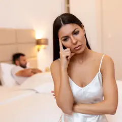 Donna pensierosa in camera da letto, mentre l'uomo è a letto. Potrebbe essere un momento per capire come aumentare la voglia di fare l'amore nell'uomo.