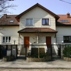 Jasny dom wielorodzinny z dwoma wejściami, ogrodzony czarnym płotem.