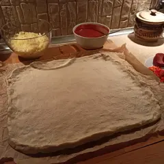Gotowe ciasto na pizzę czeka na dodatki: ser, sos, salami, papryka i oliwki.