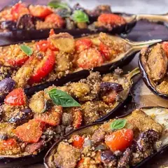Melanzane a scarpone ripiene di pomodoro, olive e pangrattato, guarnite con basilico fresco. Un piatto saporito e invitante.