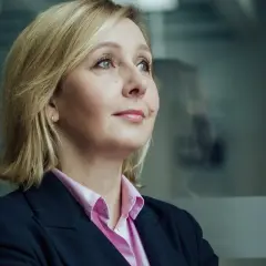 Blond polityk w różowej koszuli i granatowej marynarce patrzy w bok. W tle rozmyte sylwetki innych polityków.
