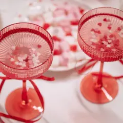 Dwa kieliszki z różowymi drinkami na walentynki, ozdobione serduszkami i wstążkami.