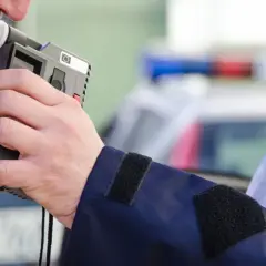 Mężczyzna dmucha w alkomat, który pokazuje wynik, mimo że nie pił. Policjant w mundurze z napisem POLICJA trzyma urządzenie.