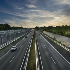 Prowadzenie pojazdu po szerokiej autostradzie, z samochodami w oddali i drzewami po bokach.