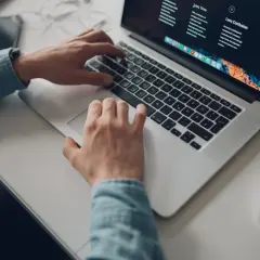 Osoba pracuje na laptopie, planując podróż z mbank konto wielowalutowe. Na biurku leży też myszka i telefon.