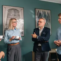Grupa osób w biurze, dyskutująca przy kawie.