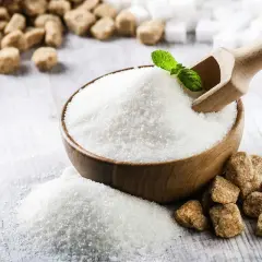 Miska z białym cukrem, drewniana łopatka z listkiem mięty, brązowy cukier i kostki cukru na drewnianym tle.