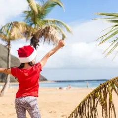Dziewczynka w czapce Mikołaja cieszy się plażą i palmami. To wyjątkowe boże narodzenie w ciepłych krajach, gdzie śnieg zastępuje piasek.