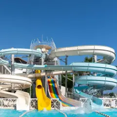 Wodne zjeżdżalnie w Orange County Alanya, z palmami i błękitnym niebem w tle, zapraszają do zabawy.