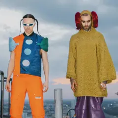 Tommy Cash i Quebonafide w ekstrawaganckich strojach na dachu. Jeden w pomarańczowo-niebieskiej kamizelce, drugi w żółtym swetrze i fioletowych spodniach.