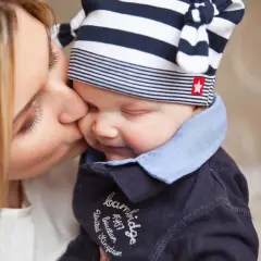 Czuła matka całuje dziecko w czapeczce. Pokazuje to sposoby radzenia sobie ze złością u dzieci, poprzez miłość i bliskość.
