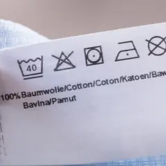 Pflegeetikett mit Waschsymbolen. Das Trockner Symbol ist durchgestrichen, was bedeutet, dass das Kleidungsstück nicht im Trockner getrocknet werden darf.