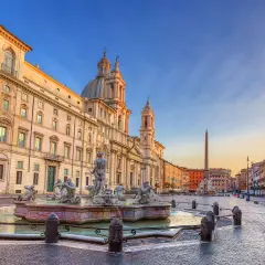 Fontana dei Quattro Fiumi e la chiesa di Sant'Agnese in Agone, simboli della piazza Navona storia, sotto un cielo al tramonto.