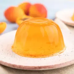 Pomarańczowa galaretka na talerzyku, obok przekrojonych brzoskwiń.