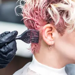 Manos enguantadas aplican tinte rosa al cabello. Si te manchas, aprende como quitar el tinte de la piel.