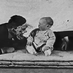 Bambino seduto, un uomo con maschera e una donna sullo sfondo, scena dall'esperimento piccolo Albert.