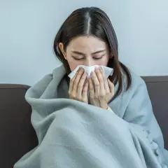 Femme enroulée dans une couverture, se mouchant. Elle cherche des conseils sur comment guerir du covid.