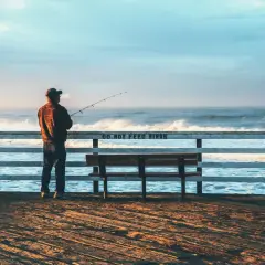 Mężczyzna z wędką na molo, cieszący się spokojnym dniem wędkarza nad wzburzonym oceanem.
