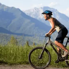Ciclista sonriente pedalea por un camino de grava con montañas al fondo. Una aventura de pirinexus gravel.