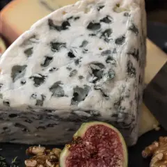 Un trozo de queso azul, con sus vetas verdes, parece un queso que huele mal. Acompañado de higos, nueces y ajo.