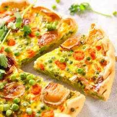 Un delicioso quiche de verduras, con guisantes, zanahoria y trozos de queso dorado, recién cortado y listo para servir.