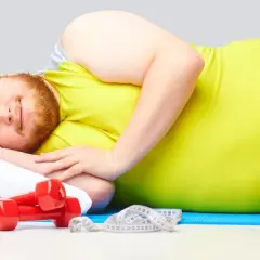 Hombre con banda roja en la cabeza, durmiendo en una colchoneta azul con pesas y cinta métrica. ¡Quizás dormir adelgaza!