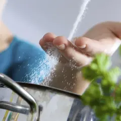 Mano espolvoreando sal fina en una olla. La sal es el mejor sal para cocinar y realza los sabores.